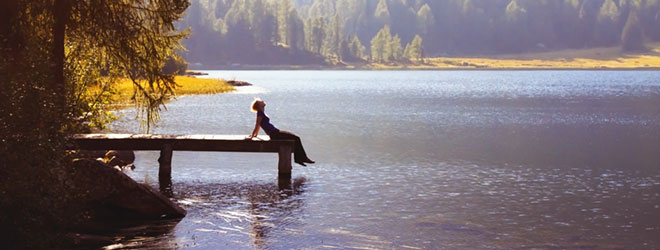 Person sitting at the end of a dock in scenic surroundings; QAI helps protect the environment through organic certification.